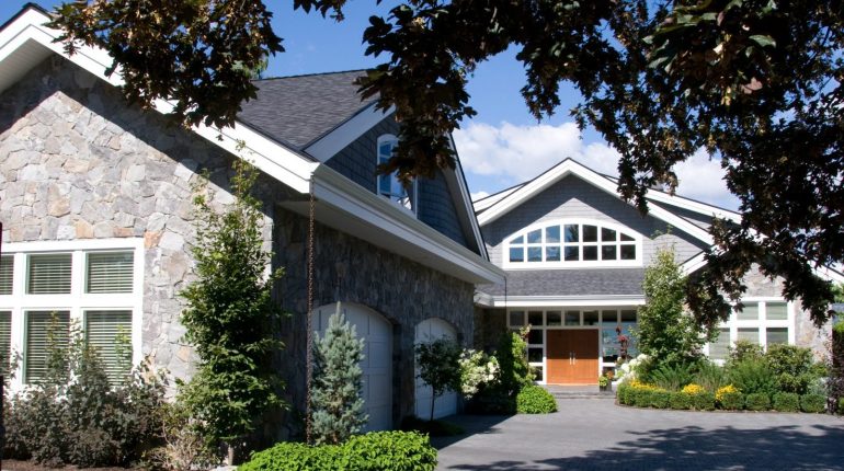 Large stone suburban house with lots of plants