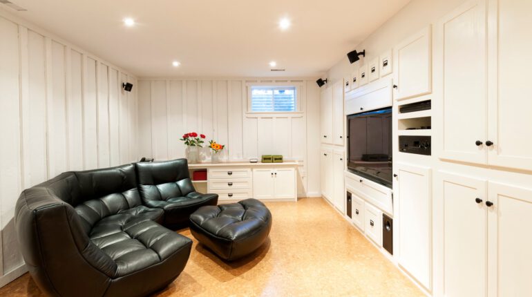 Stock image of entertainment room basement with large black leather couch